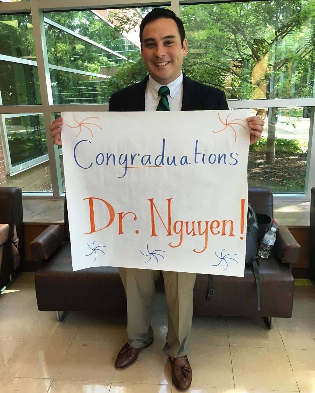Dr. Nguyen holding sign congratulating him on graduating